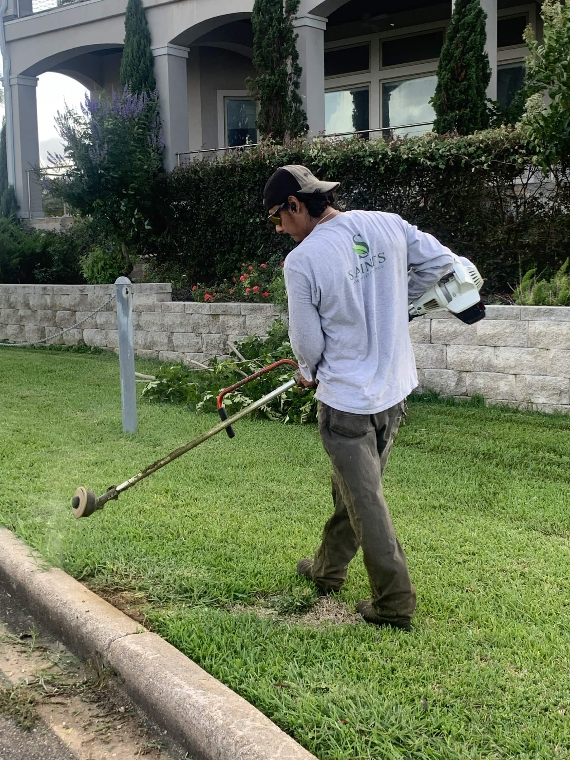 Saints Lawn Maintenance worker trimming lawn edges beside a residential property